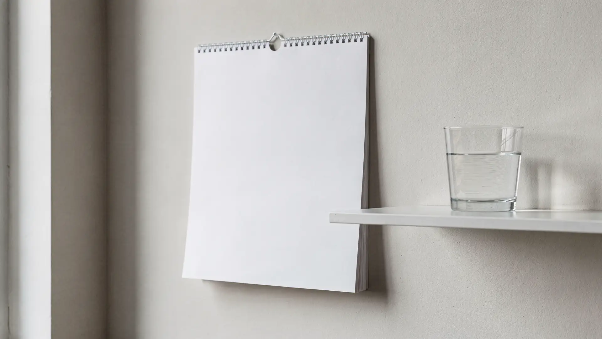 Calendario de parede em branco ao lado de prateleira com copo de agua em luz natural, cena sobre o que fazer ao esquecer uma dose