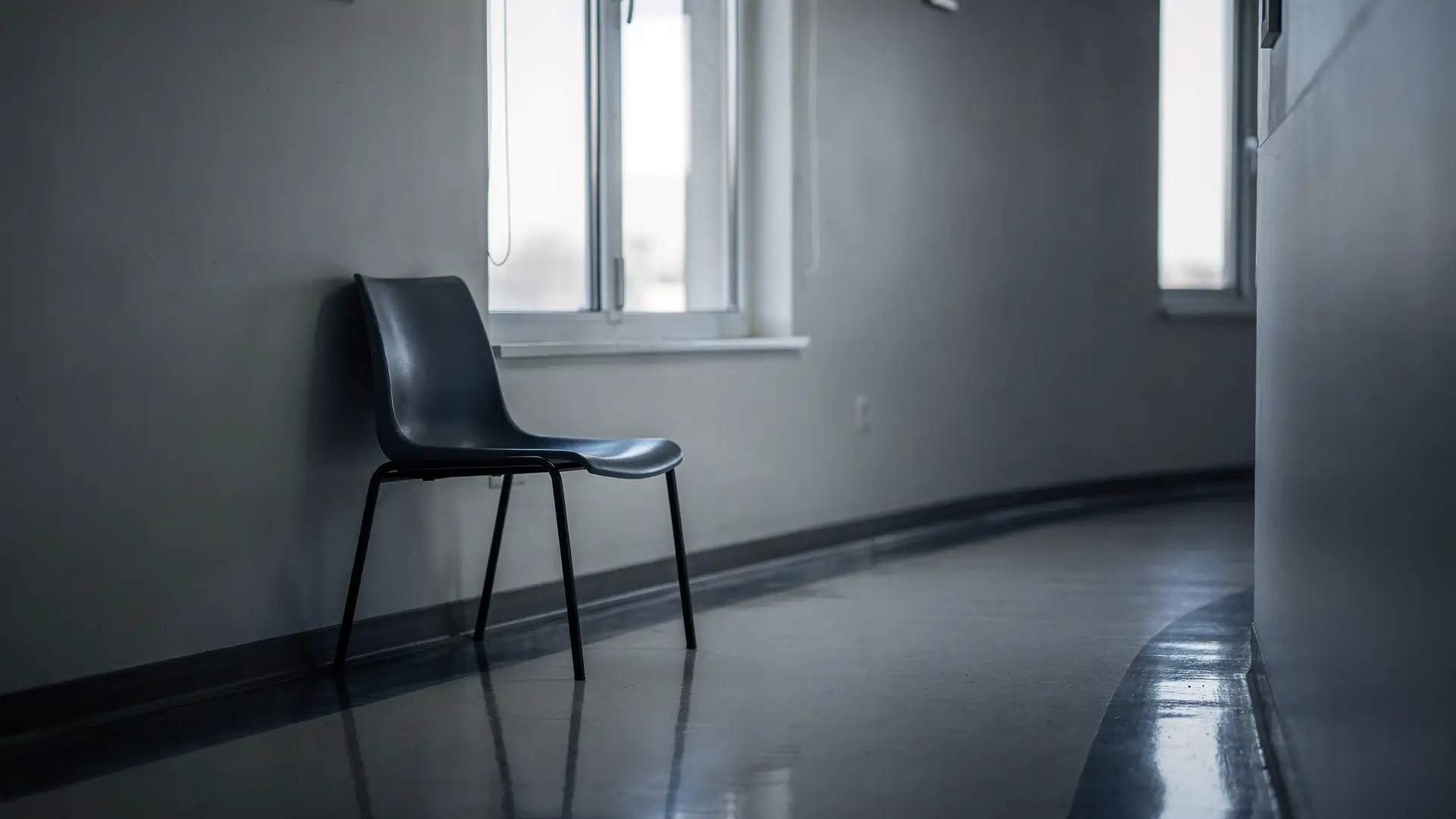 Cadeira de espera vazia em corredor de pronto atendimento com luz fria vinda de janela alta, cena sobre o sinal de dor que pede avaliacao no mesmo dia