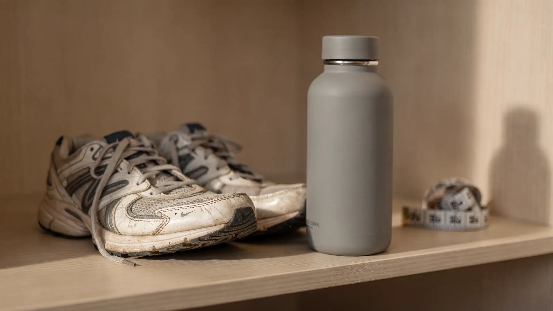 Tenis de corrida e garrafa de agua em primeiro plano com fita metrica desfocada ao fundo, cena sobre trocar o numero da balanca por outros sinais de progresso